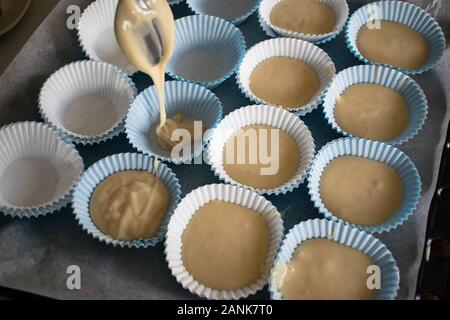 Il riempimento degli stampi di carta con la pasta per fare i muffin Foto Stock