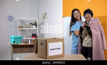 Lieto di volontari e senzatetto femmina fotocamera sorridente, donazione nel centro sociale Foto Stock