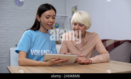 Assistente sociale aiutando senior lady di far fronte con la compressa, l'insegnamento delle nuove tecnologie Foto Stock