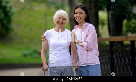 Nonna con telaio a piedi e giovani femmine abbracciando e sorridente in telecamera Foto Stock