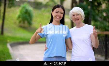 Volontari femmina e donna anziana che mostra Thumbs up, sociale progetto di supporto Foto Stock