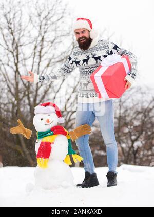 Sogni. Felice hipster pronto per natale. vacanze inverno. un maglione pesante a basse temperature. santa uomo dare presente all'esterno. l'uomo barbuto costruire pupazzo di neve. stagione invernale attività. Auguri di Buon Natale. Foto Stock