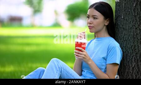 Felice femmina limonata potabile attraverso la paglia seduta albero giardino, ristoro Foto Stock