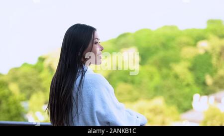 Signora giovane indossare accappatoio bianco godendo di mattina all'aperto sulla terrazza dell'albergo Foto Stock