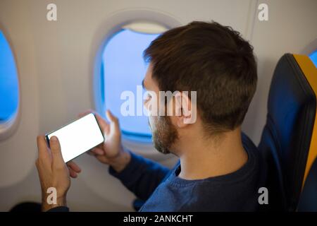 Mockup aereo dello smartphone. Attraente giovane uomo europeo tenendo premuto lo schermo è vuoto smartphone nelle mani in aereo. Mock up per un gioco mobile application Foto Stock