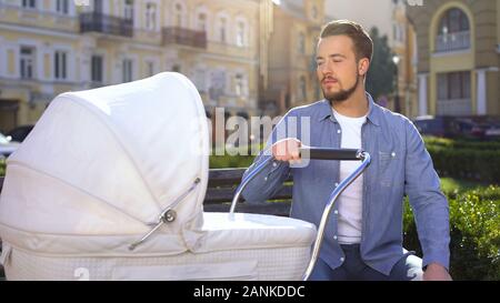 Stanco di sleepy uomo passeggino oscillante seduta su una panchina nel parco, la genitorialità esaurimento Foto Stock