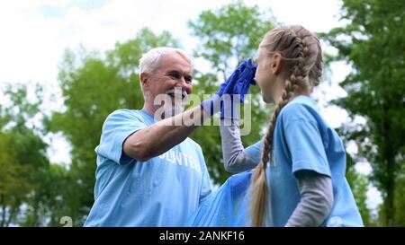 Sorridenti volontari anziani con il nipote raccogliere rifiuti dando alta cinque Foto Stock