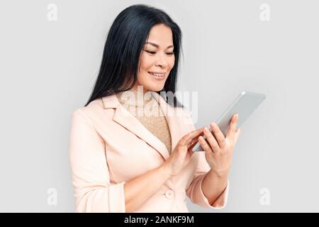 Freestyle. Imprenditrice asiatici in piedi isolato su bianco con tavoletta digitale navigando su internet allegro Foto Stock