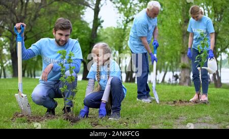 Felice famiglia volontari piantare alberelli all'aperto godendo fece del lavoro Foto Stock