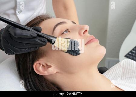 Tagliato in prossimità di un cosmetologo applicando nero maschera sul volto di una bella donna matura Foto Stock