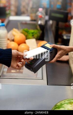 Spesa giornaliera. Uomo in piedi al supermercato contatore del cassiere di pagare per gli acquisti con lo smartphone contactless close-up Foto Stock