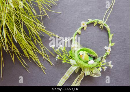 Composizione primaverile con una corona intrecciata di ramoscelli con fiori di ciliegio, uccello decorativo e uovo di Pasqua su uno sfondo grigio pianura Foto Stock