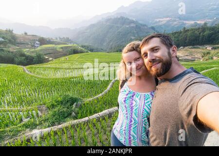 Giovane coppia caucasica rendendo selfie e sorridente a terrazze di riso di Sapa a Lao Cai regione del Vietnam. Foto Stock