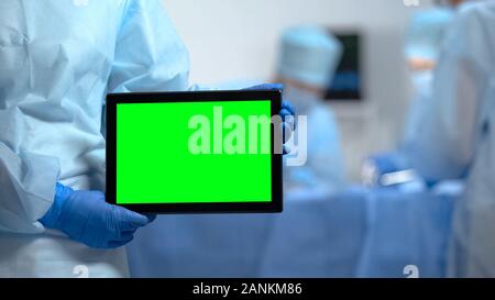 Le mani di infermiere azienda tablet PC con schermo verde durante il funzionamento dell'ospedale Foto Stock