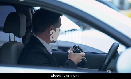 Agente privato con fotocamera seduti in auto, la ricerca di prove di barare Foto Stock