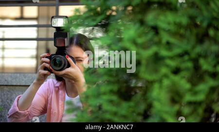 Paparazzi femmina nascosto dietro gli alberi di scattare le foto alla ricerca di sensazione Foto Stock