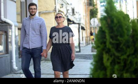 Donna matura camminando sulla strada con uomini più giovani, le relazioni e il collegamento Foto Stock