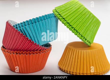 Stretto shot di coloratissimi cupcake wrappers impilati in due pile su sfondo bianco Foto Stock