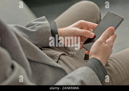 Giovane uomo guarda la schermata Telefono. l uomo detiene smartphone e si siede in reti sociali Foto Stock