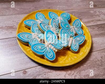 Abstract blue butterfly cookies delineato con una spessa glassa reale su una piastra di colore giallo e impostare su sfondo di legno Foto Stock