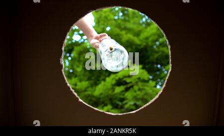 Mettendo mano una bottiglia di vetro nel contenitore per materiali riutilizzabili, rifiuti riutilizzabili Foto Stock