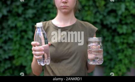 Donna scegliendo tra la tazza di vetro e la bottiglia di plastica, ambiente risparmio Foto Stock