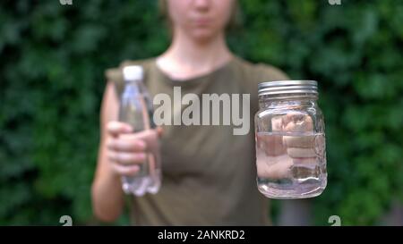 Signora mostra tazza di vetro per fotocamera, preferendola alla bottiglia di plastica, salvataggio di messa a terra Foto Stock