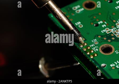 Immagine macro di un ferro da saldatore punta essendo applicato ad una connessione di componenti su una scheda a circuito stampato apparentemente per de-la saldatura su una superficie riflettente Foto Stock