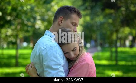 L'uomo abbracciando e consolante sconvolto ragazza nel parco, stare insieme e il supporto Foto Stock