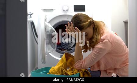 Stanco donna abiti di caricamento in macchina di lavaggio, infastiditi con routine di faccende di casa Foto Stock