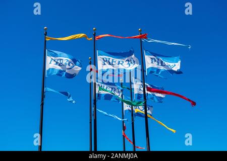 Pier 39 bandiere multicolori in cielo blu sbattimenti nel vento pubblicità ad un centro commerciale e popolare attrazione turistica sulla storica Embarcadero Foto Stock