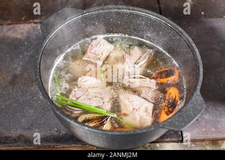 chef cuoco aggiunge gli ingredienti. brodo di manzo tradizionale con verdure, ossa e ingredienti in pentola, ricetta di cottura. Zuppa in una pentola di cottura con mestolo Foto Stock