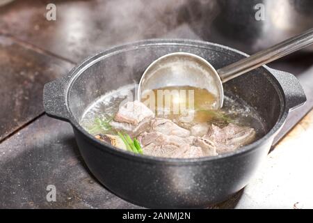 chef cuoco aggiunge gli ingredienti. brodo di manzo tradizionale con verdure, ossa e ingredienti in pentola, ricetta di cottura. Zuppa in una pentola di cottura con mestolo Foto Stock