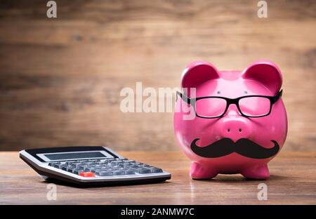 Rosa Piggybank con la Calcolatrice sul tavolo di legno Foto Stock