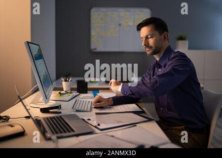 Imprenditore guardando a guardare mentre si lavora fino a tardi in ufficio Foto Stock
