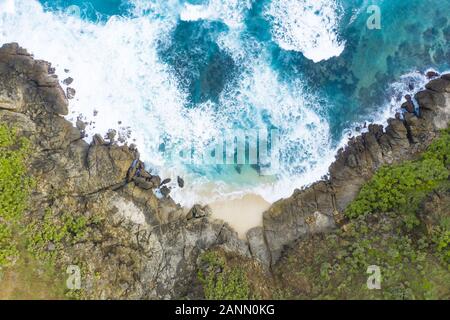 Incredibile vista aerea di un nascosto spiaggia bagnata da un mare turchese e affiancata da un verde scogliera rocciosa. Isola di Lombok, West Nusa Tenggara, Indonesia. Foto Stock