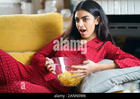 Il persiano donna a casa a guardare la TV mangiando patate chips Foto Stock