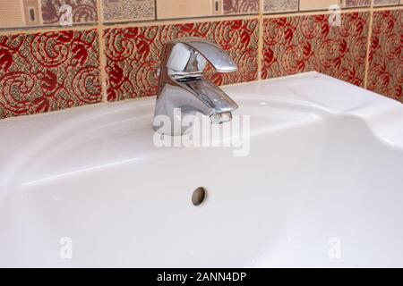 Shiny Silver residenziale bagno rubinetto o toccare una ceramica bianca lavabo. Plumbing, DIY, o concetti di manutenzione. Foto Stock