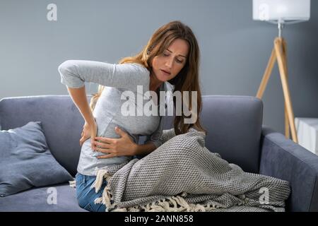 Donna matura avente un mal di schiena mentre è seduto sul divano Foto Stock