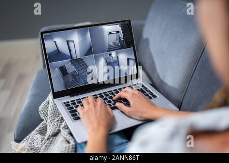 Close-up di donna seduta sul divano di casa di monitoraggio di telecamere di sicurezza sul portatile a casa Foto Stock