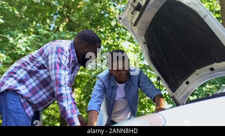 Papà nero lodando il nostro figlio adolescente learning per la riparazione auto, famiglia stare insieme Foto Stock