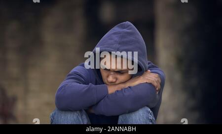 Disperata giovane uomo seduto street da soli, violenza domestica in esecuzione da casa Foto Stock
