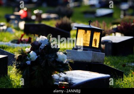 Grave lanterna con vetro giallo splendente nella luce posteriore su una lapide in un cimitero contro sfondo sfocato Foto Stock