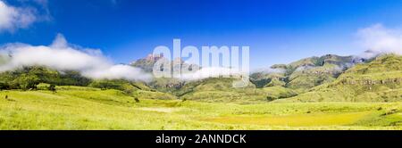 Panorama di montagne Drakensberg come Cathkin Peak, del fratello cappottatura e Champagne Castle con morbide e lussureggianti prati verdi e un cielo blu, Sud Afri Foto Stock