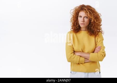 Sospetto, allarmati e addolorato redhead curly fidanzata in felpa gialla, accigliata e strizzare gli occhi come guardano con diffidenza i bracci incrociati su petto, Foto Stock