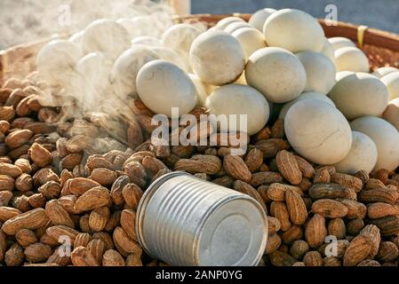 Close-up di arachidi cotti al vapore e bianco uova sode per la vendita su un nativo di vassoio di bambù con una coppa di misurazione, visto nelle Filippine a tardo pomeriggio Foto Stock