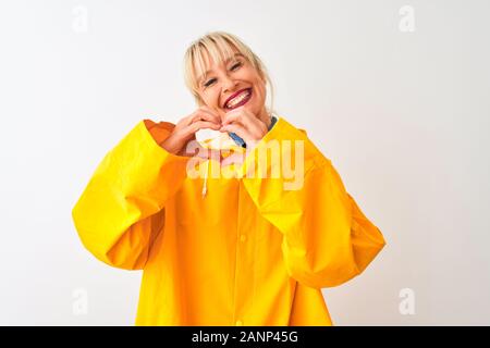 Medioevo donna che indossa il giallo cappotto di pioggia in piedi isolato su sfondo bianco sorridente in amore che mostra il simbolo del cuore e la forma con le mani. Romantico Foto Stock