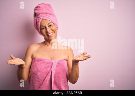 Medioevo donna che indossa asciugamano da bagno dalla bellezza cura del corpo su sfondo rosa clueless e espressione confusa con le braccia e le mani alzate. Dubbio conc Foto Stock