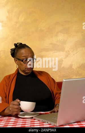 Una donna che beve una tazza di caffè mentre si trova su un computer portatile in un Internet cafè stock Foto Stock