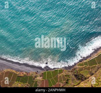 Paesaggio di antenna dal blu oceano Atlantico. Spiaggia di pietra e campi adiacenti sulla costa meridionale dell'isola di Madeira, Portogallo. Foto Stock